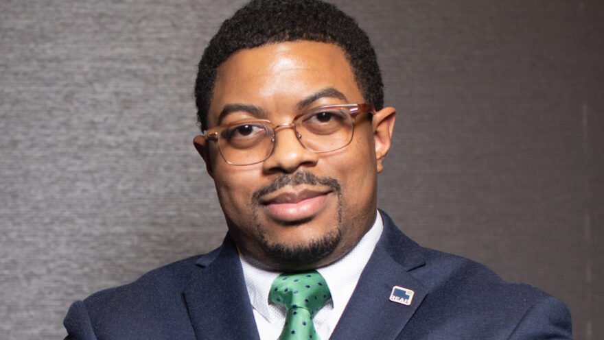 Photo of Jon Petty in a blue suit in front of a gray wall