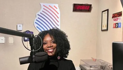 Ruby Mendenhall smiling at the camera with microphone in front of her.