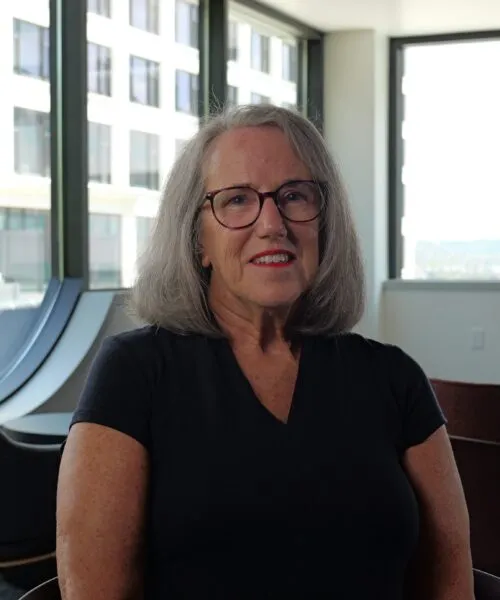 Photo of Kathie Brown in an office in front of windows in a black dress