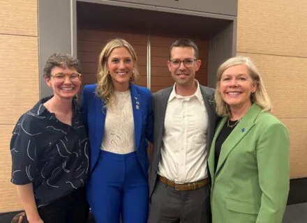 Photo of four MUP graduates in front of a yellow wall