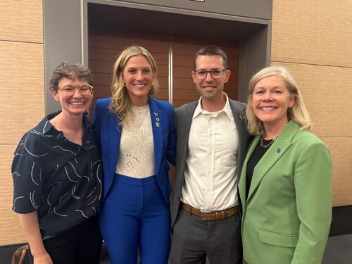 Photo of four MUP graduates in front of a yellow wall