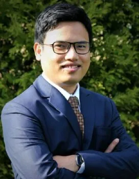 Photo of Shuvangkor Shusmoy Roy in front of tree wearing blue suit