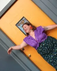 person leans against yellow door with arms out
