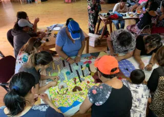 several people gathered around a table sewing a textile