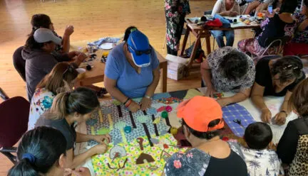 several people gathered around a table sewing a textile