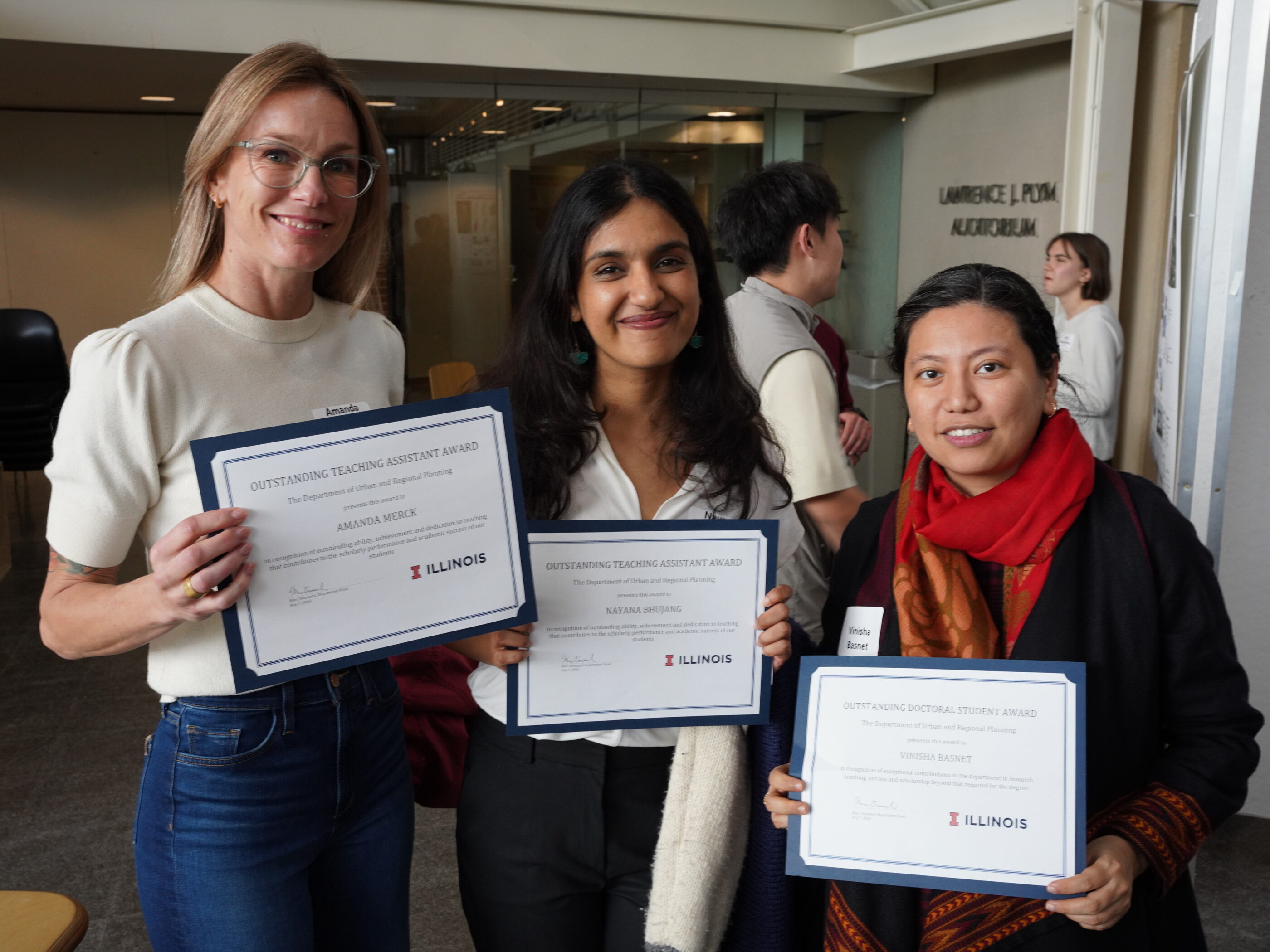 three people smile while holding award certificates