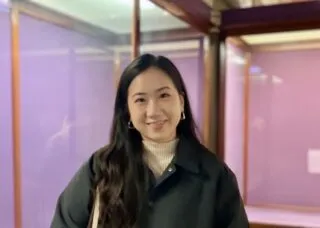 Photo of Nadia Kim in front of pink walls wearing a dark green coat