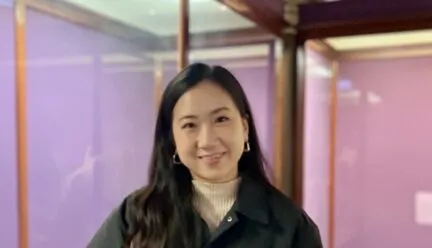 Photo of Nadia Kim in front of pink walls wearing a dark green coat