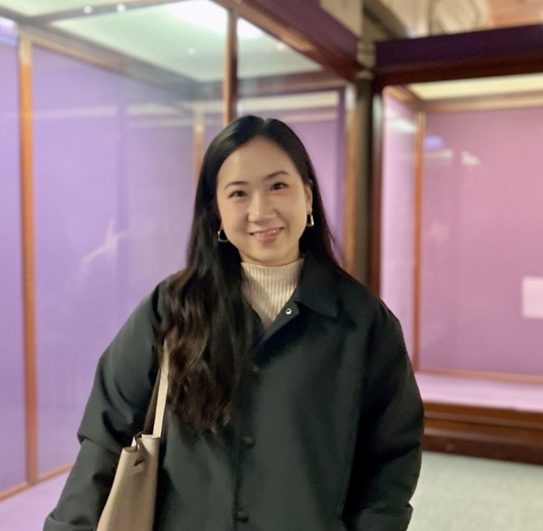 Photo of Nadia Kim in front of pink walls wearing a dark green coat