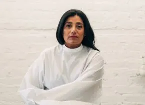 Suchi Reddy seated against a white brick background 