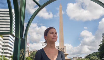 Elisa Silva staring off into distance, surrounded by unique architecture, blue sky and white clouds