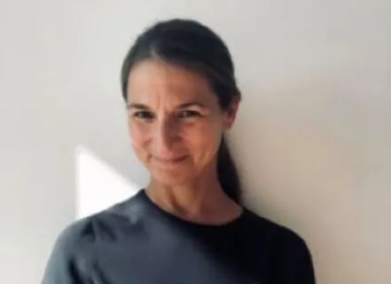 Elisa Silva looking off into the distance, blue sky and white clouds behind her, surrounded by unique architecture