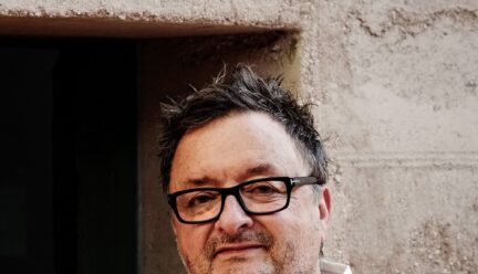 Rick Joy wearing a button up white shirt, black framed glasses, not shaven