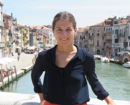 Elsa Silva standing in Italy on bridge in front of apartments