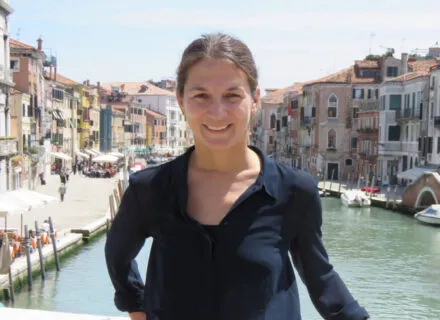 Elisa Silva in Italy, standing a bridge in front of houses, river inbetween