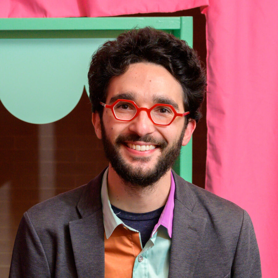 a smiling man wearing abstract colors and red rimmed glasses