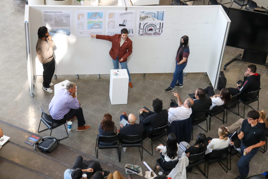 pic of student presenting with a model in front on a white stand and work pinned up behind them