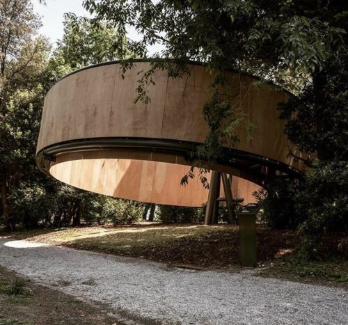 circular wooden building angled off the ground without a roof 