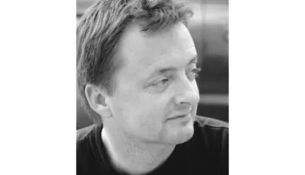 man with short hair black tshirt looking to his left as camera photographs, picture is black and white