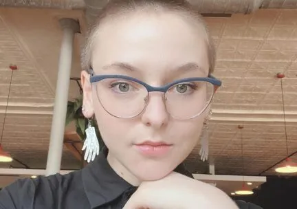 bald woman big earings blue framed glasses looking at a camera