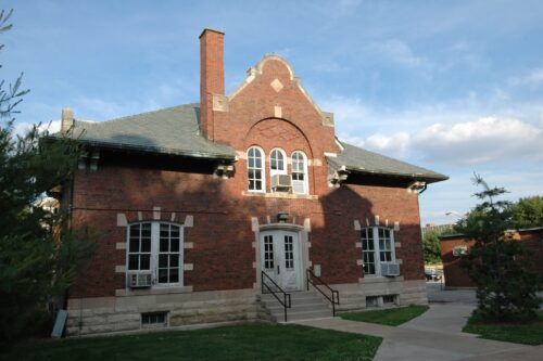 picture of the outside of architecture annex with 7 windows, a chimnew, stairs up to double doors that are white