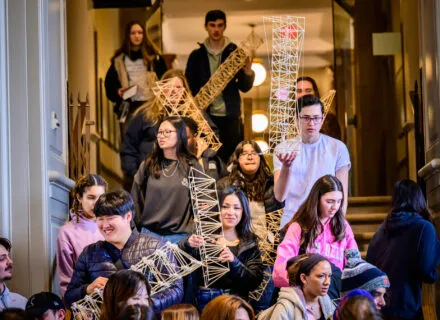 several students walking into the architecture studio holding trusses