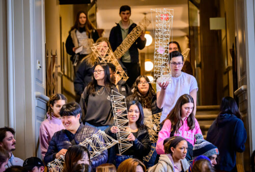 several students walking into the architecture studio holding trusses