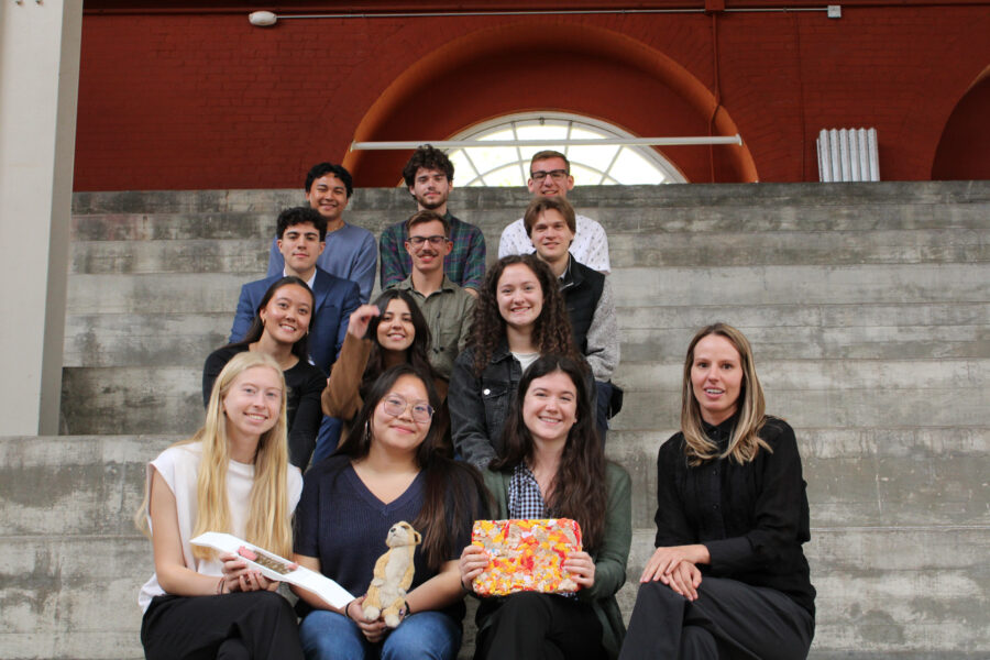 12 students with their professor sitting on steps at the stock pavilion holding their models