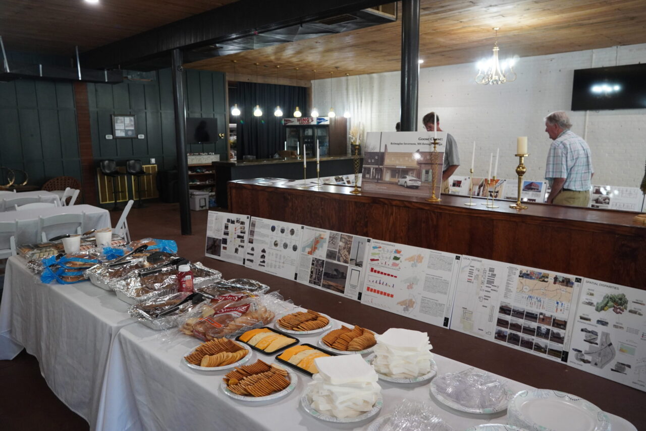 Architecture drawings placed against a wall behind a table filled with food. 
