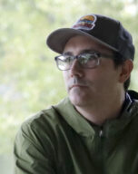 Portrait of Ryan Griffis in an outdoor setting, wearing a baseball hat and green rain jacket.