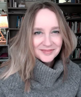 Portrait of Molly Briggs in a gray turtleneck sweater in front of bookshelves