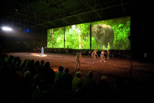 Performance view of the Unreliable Bestiary showing projection, performers, and audience