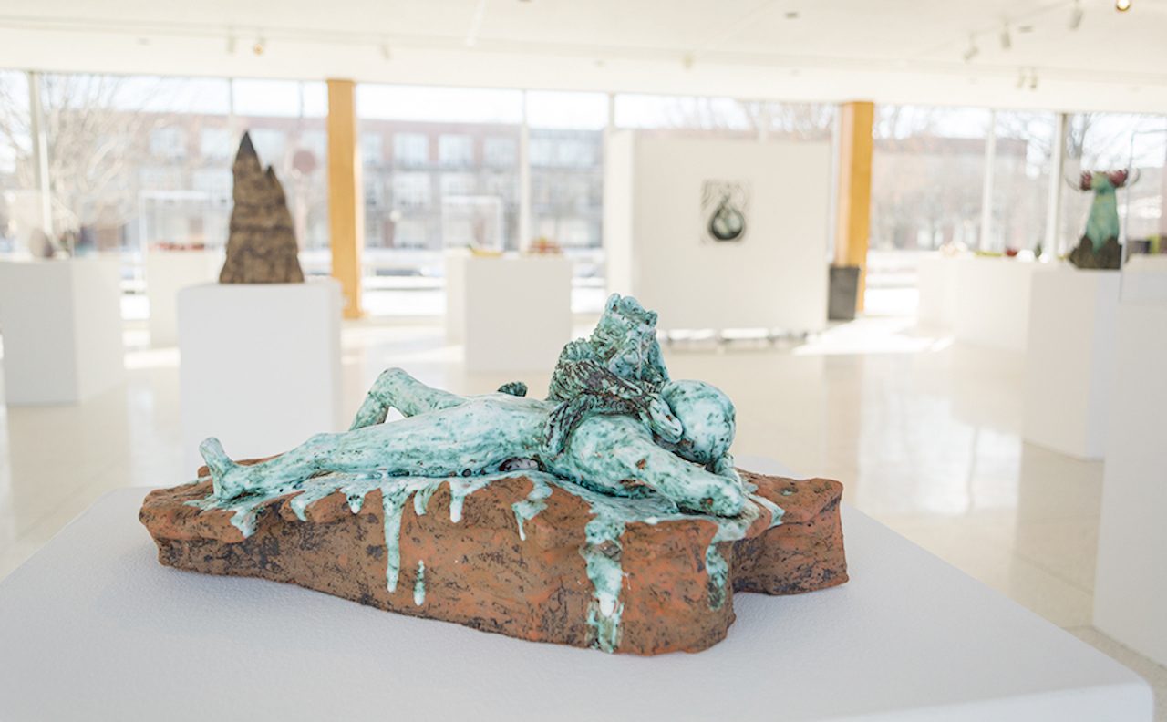Photo of a ceramic artwork of a figure glazed in variegated green reclining on a unglazed ceramicplinth