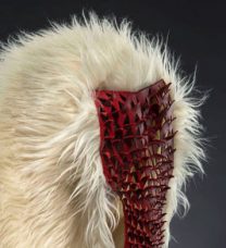 Photo of an artwork with a red mask-like form laid over a white fur hood-like form