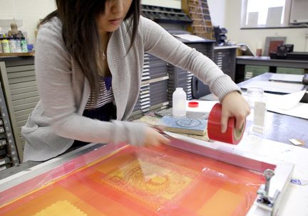 Photo of a student printing from a red and orange silkscreen