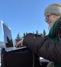 在冬季风景中，微笑的学生在户外用笔记本电脑工作的肖像