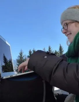 Portrait of the smiling student working on a laptop outdoors in a winter landscape