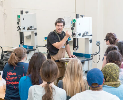 staff member instructs group of students on use of bandsaw