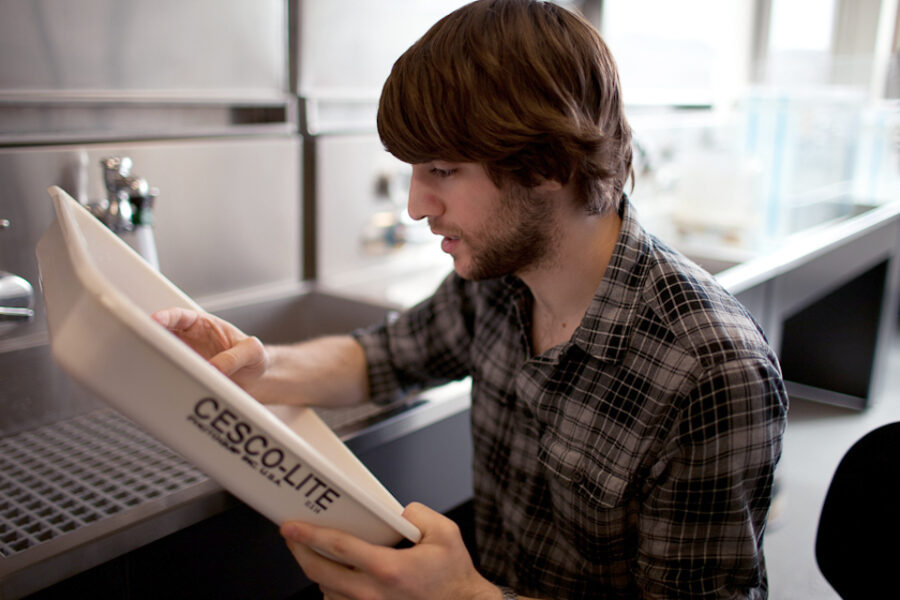 student inspects print in a white tray in front of darkroom sinks