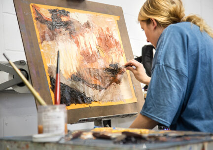 photo of a female student painting and abstract image on canvas taped to a board