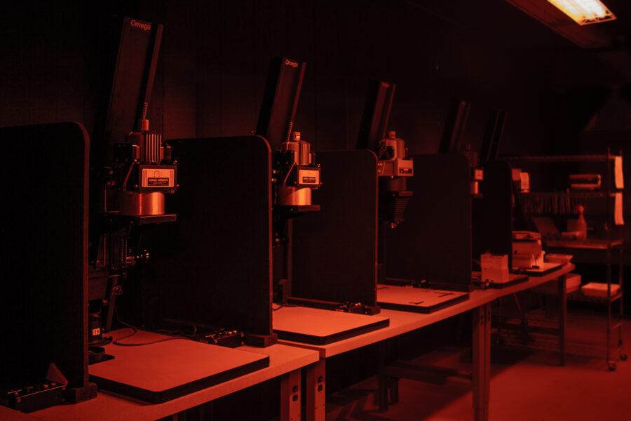 row of enlargers in darkroom under red safe lights