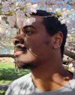 Portrait of the alumnus in profile beneath a flowering spring tree