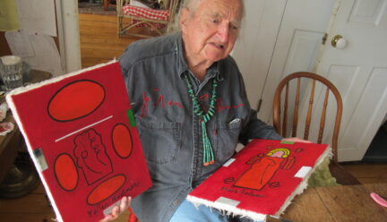 Peter Bodnar sitting on chair holding two of his paintings in bold red