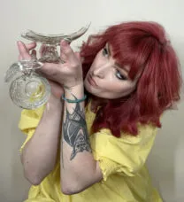 Portrait of Erica FItzgerald holding a broken, domestic glass bowl above and close to her face while looking up at it.