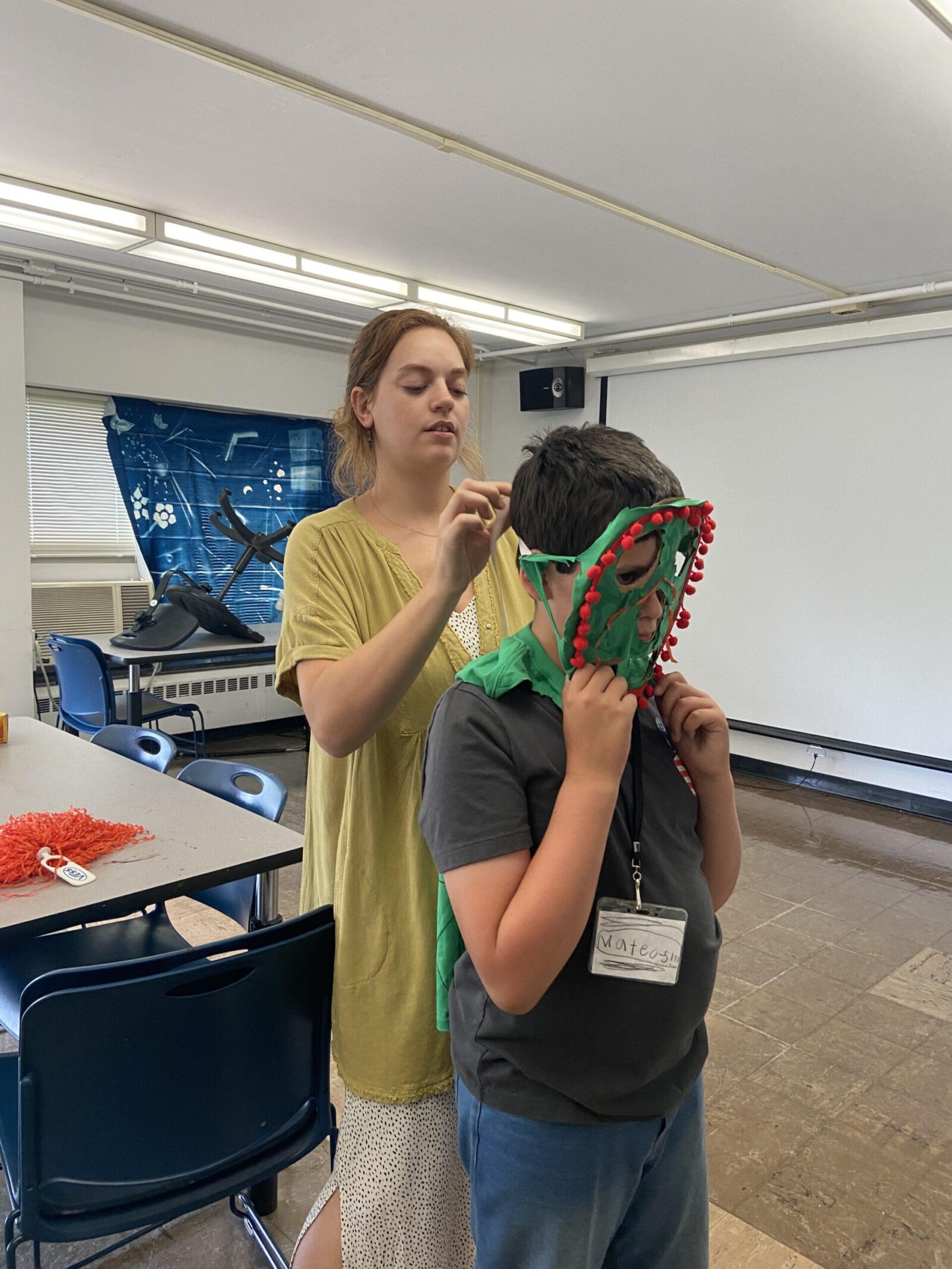 a teacher helping a student put on a mask they made