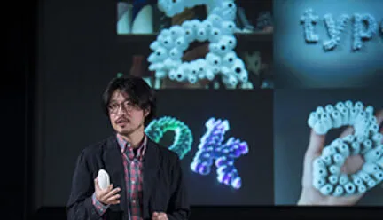 Lee giving a lecture with photos of work in background