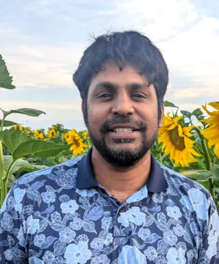 Sharath smiling in a sunflower field