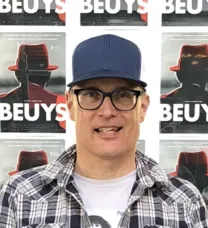 man in cap in front of Beuys posters