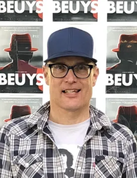 man in cap in front of Beuys posters