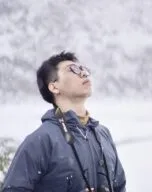 Portrait of a man standing in a snowy landscape with closed eyes holding a camera and snow falling 